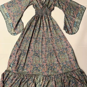 May include: A long, flowing maxi dress with a paisley print in shades of blue, green, and pink. The dress has a V-neckline, long sleeves, and a ruffled hem.