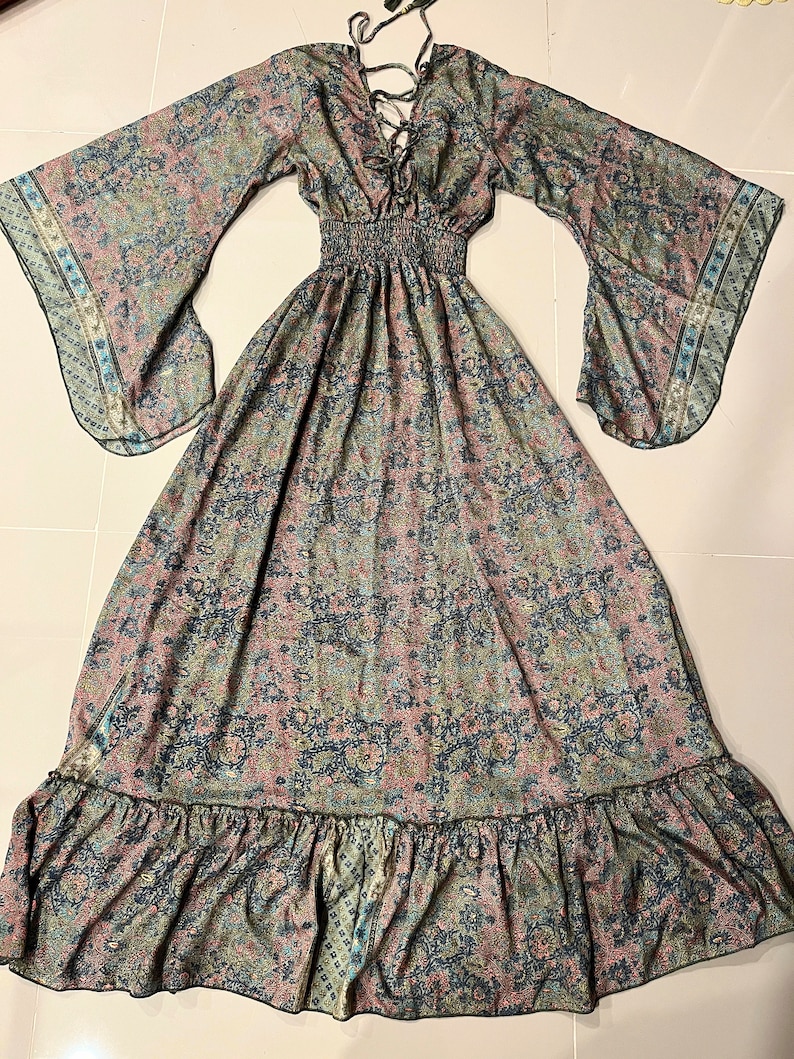 May include: A long, flowing maxi dress with a paisley print in shades of blue, green, and pink. The dress has a V-neckline, long sleeves, and a ruffled hem.
