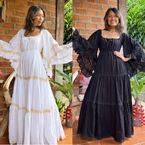 May include: Two women wearing long, flowing dresses with ruffled sleeves and tiered skirts. The dress on the left is white with gold trim, and the dress on the right is black with black trim.