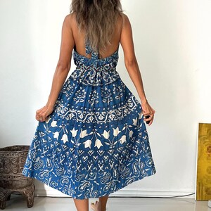 May include: A blue and white floral print maxi dress with a halter neckline and a tie back. The dress has a tiered skirt and a relaxed fit.