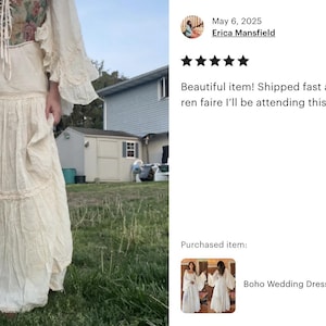 May include: A white maxi dress with a lace trim and a floral pattern on the bodice. The dress has a flowing skirt and long sleeves with ruffles. The dress is photographed outdoors in a grassy area.