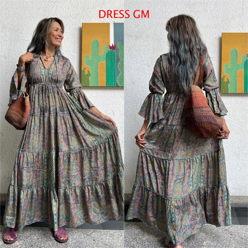 May include: A long, tiered, floral print dress with a V-neckline and long sleeves. The dress has a relaxed fit and a flowy silhouette. The model is wearing the dress with a brown bag.