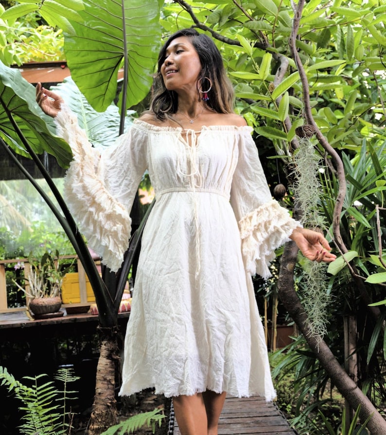 May include: A white off-the-shoulder dress with long, ruffled sleeves and a tie at the neckline. The dress is made of a lightweight fabric and has a flowy silhouette.