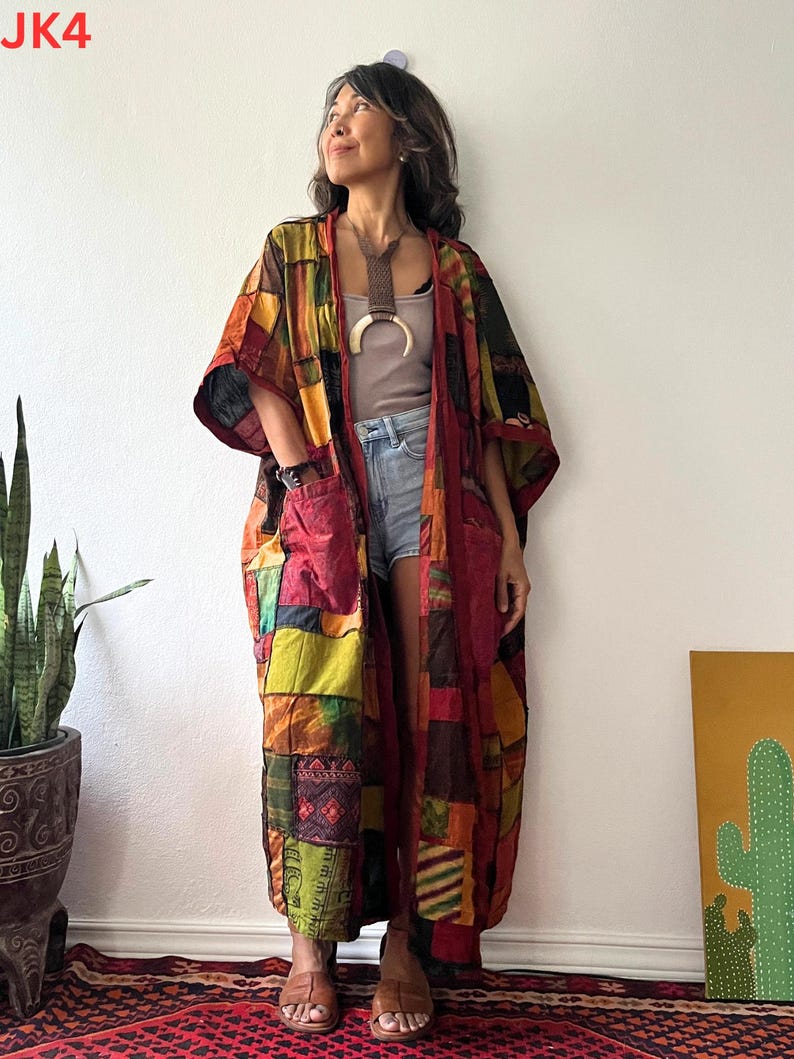 May include: A long, open-front kimono robe featuring a patchwork design with various fabric squares in shades of red, orange, yellow, green, and brown. The garment includes two large front pockets and wide sleeves, worn over a neutral top and denim shorts.