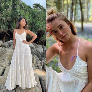 Puede incluir: Dos mujeres con vestidos blancos, sueltos y sin mangas. La mujer de la izquierda est&aacute; de pie en una playa rocosa. La mujer de la derecha est&aacute; de pie en un bosque con flores moradas.