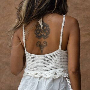 May include: Cream-coloured crochet top with a layered design and spaghetti straps. The top has a textured crochet bodice and an embroidered bottom layer. The back of the top is visible, and the style is bohemian.