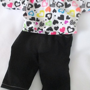 May include: A white short-sleeved shirt with a colorful heart print and black pants.