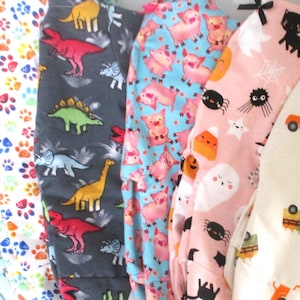 May include: A collection of six pairs of colorful pajamas with various patterns, including paw prints, dinosaurs, pigs, and trucks. The pajamas are made of soft, comfortable fabric and are perfect for lounging around the house.