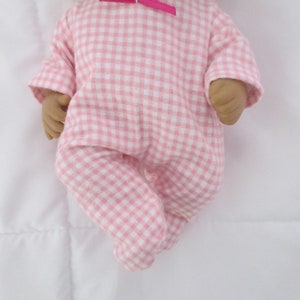 May include: A pink and white gingham baby doll onesie with a pink bow at the neckline.