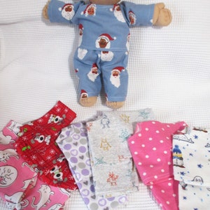 May include: A Cabbage Patch Kid doll wearing blue pajamas with a Santa Claus print. The doll is surrounded by six different fabric scraps, each with a different pattern, including red with white snowflakes, pink with white polka dots, gray with robots, purple with white polka dots, white with blue stars, and white with blue penguins.