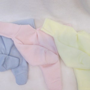 May include: Three baby onesies in different colors: light blue, pink, and yellow. The onesies are made of soft fleece material and have long sleeves.