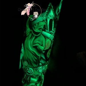 Puede incluir: Un vaso verde que brilla en la oscuridad con un dise&ntilde;o de Jack Skellington de la pel&iacute;cula Pesadilla antes de Navidad. El vaso presenta a Jack Skellington sosteniendo una calabaza con una casa encantada en el fondo.