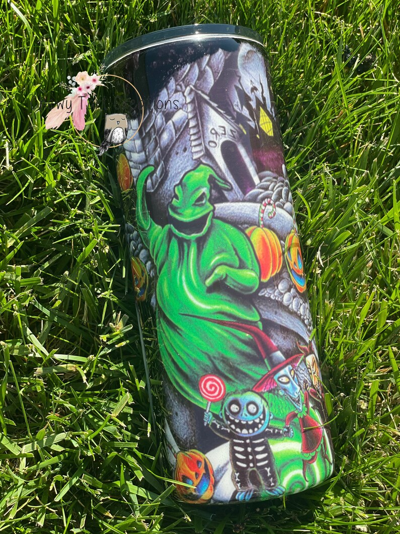 Puede incluir: Un vaso negro y verde con un dise&ntilde;o de tem&aacute;tica de Halloween. El dise&ntilde;o presenta un fantasma verde, un esqueleto y una calabaza. El vaso tiene una tapa negra.