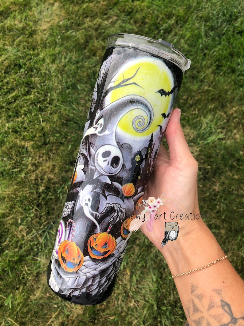 Puede incluir: Un vaso negro y blanco con un dise&ntilde;o de Pesadilla Antes de Navidad. El dise&ntilde;o presenta a Jack Skellington, Sally y otros personajes de la pel&iacute;cula. El vaso est&aacute; decorado con purpurina y tiene una tapa transparente.