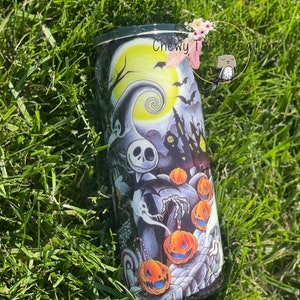 Puede incluir: Un vaso negro y blanco con un dise&ntilde;o de Pesadilla Antes de Navidad. El dise&ntilde;o presenta a Jack Skellington, Sally y calabazas. El vaso tiene una tapa negra y una base blanca.