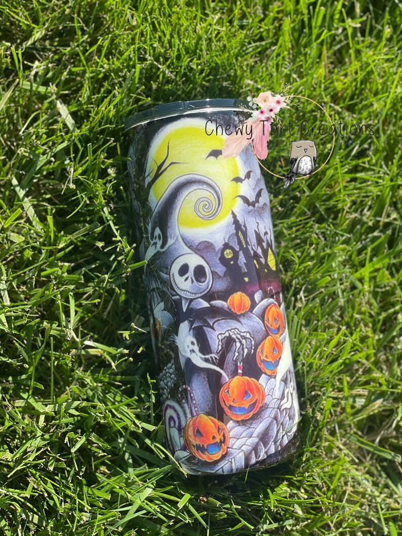 Puede incluir: Un vaso negro y blanco con un dise&ntilde;o de Pesadilla Antes de Navidad. El dise&ntilde;o presenta a Jack Skellington, Sally y calabazas. El vaso tiene una tapa negra y una base blanca.