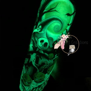 Puede incluir: Un tatuaje temporal que brilla en la oscuridad con un dise&ntilde;o verde de Jack Skellington de la pel&iacute;cula "Pesadilla antes de Navidad". El tatuaje incluye una luna llena, un &aacute;rbol espeluznante y calabazas. El tatuaje est&aacute; en el brazo de una persona.