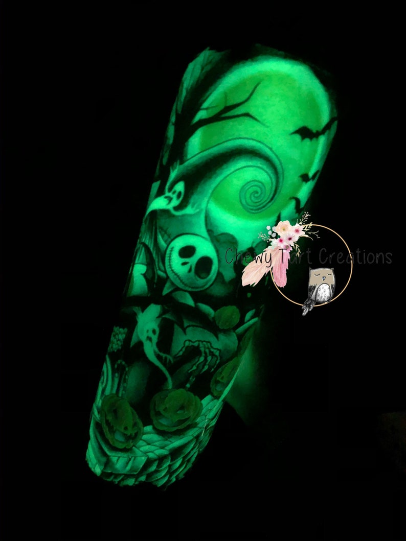 Puede incluir: Un tatuaje temporal que brilla en la oscuridad con un dise&ntilde;o verde de Jack Skellington de la pel&iacute;cula "Pesadilla antes de Navidad". El tatuaje incluye una luna llena, un &aacute;rbol espeluznante y calabazas. El tatuaje est&aacute; en el brazo de una persona.