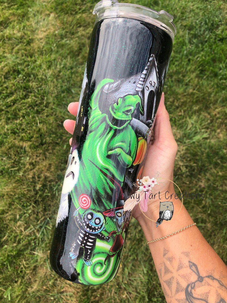 Puede incluir: Un vaso de acero inoxidable negro y verde con acabado brillante. El vaso presenta un gr&aacute;fico de personajes de Pesadilla antes de Navidad, incluyendo a Jack Skellington, Sally y el Fantasma de las Navidades Presentes. El texto "Chewy Tart Creations" es visible en el vaso.