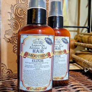 以下が含まれることがあります： Zir Yabs Leave-On Amino Acid Hair Smoothing Elixirの茶色のボトルが2本。各60 ml。ボトルには黒いポンプと製品情報が記載されたラベルが付いています。背景は織り込まれた表面です。