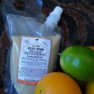 May include: A clear plastic pouch with a white cap filled with a light brown liquid. The pouch is labeled "Zir Yabs Body Brew Mineral Deodorant Citrus Roll On" and lists ingredients, directions, and a website. The pouch is sitting on a brown surface with a green lime and an orange.