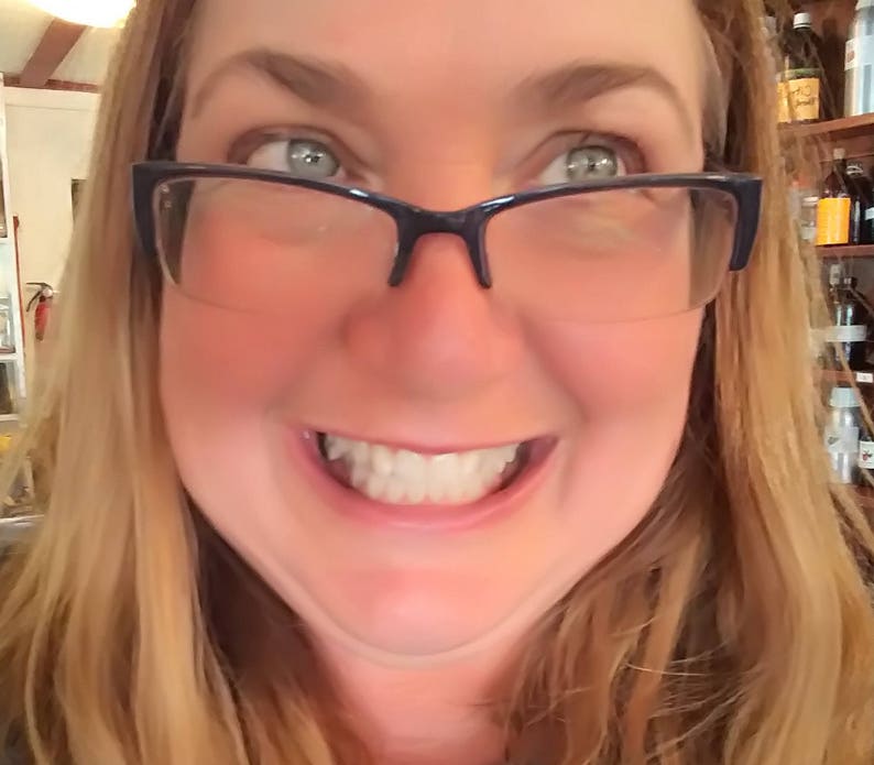 Peut inclure: Une femme aux cheveux blonds portant des lunettes sourit largement, montrant ses dents. Ses cheveux sont s&eacute;par&eacute;s sur le c&ocirc;t&eacute; et tombent sur ses &eacute;paules. Elle porte des lunettes &agrave; monture noire.