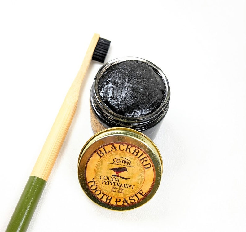 Peut inclure: Un pot de dentifrice Blackbird Cocoa Peppermint noir et or avec une brosse &agrave; dents noire en arri&egrave;re-plan.