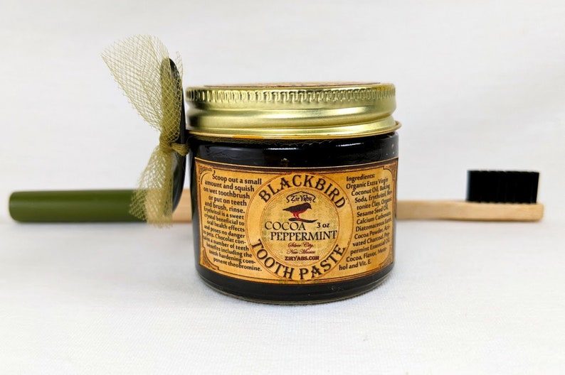 Peut inclure: Un pot de dentifrice Blackbird &agrave; la menthe poivr&eacute;e et au cacao de 3 oz. Le pot est noir avec un couvercle dor&eacute; et une &eacute;tiquette illustrant un merle. L'&eacute;tiquette comprend &eacute;galement le texte "Blackbird", "Cocoa Peppermint", "3 oz", "Toothpaste", et "Ziryabs.com".