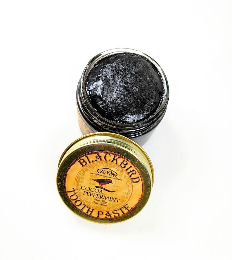 Peut inclure: Un pot dor&eacute; avec un couvercle noir contenant du dentifrice noir. Le couvercle porte une &eacute;tiquette qui dit "Blackbird" avec une petite illustration d'oiseau et le texte "Cocoa Peppermint Tooth Paste".