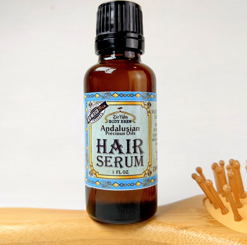 Pu&ograve; includere: Una bottiglia di vetro marrone con un tappo nero, etichettata "Zir Yabs Body Brew Andalusian Precious Oils Hair Serum 1 FL OZ".