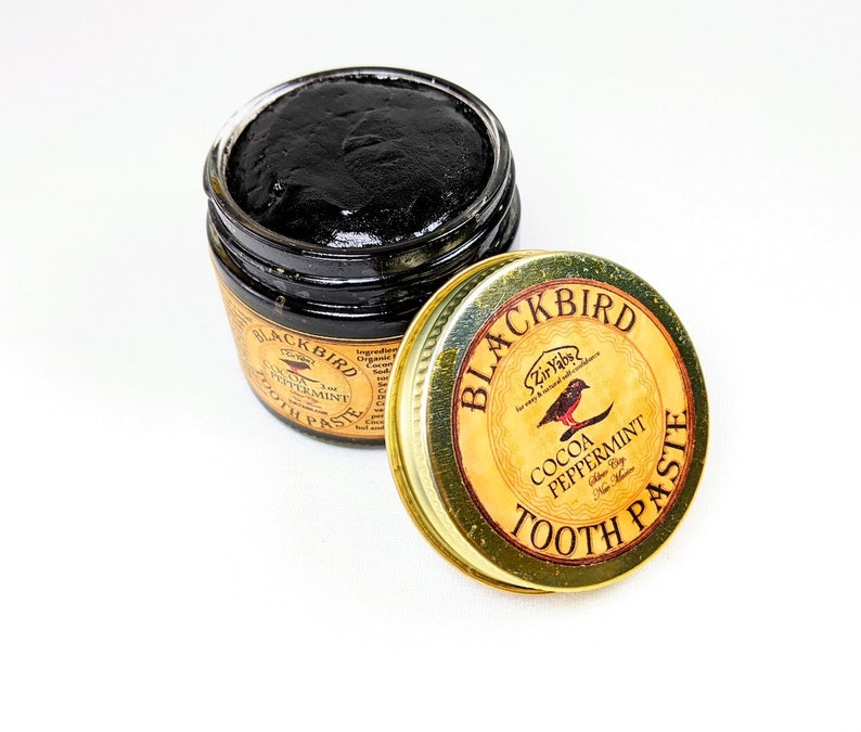 Peut inclure: Un pot en verre de dentifrice au charbon de bois noir avec un couvercle dor&eacute;. Le couvercle porte le texte "Blackbird Zir Vabs for easy & natural teeth care" et "Cocoa Peppermint Tooth Paste".