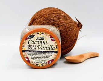 May include: A jar of coconut vanilla sugar scrub with a brown coconut and a wooden spoon beside it. The jar has an orange lid with the text "Zir Yabs Body Brew Coconut Sugar Scrub Vanilla" and "Great for hands, face, elbows and more!" The text on the jar also lists the ingredients.