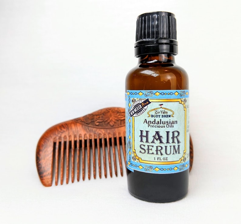 Pu&ograve; includere: Una bottiglia di vetro marrone con un tappo nero e un'etichetta blu e bianca che recita "Zir Yaby Body Brew Andalusian Precious Oils Hair Serum 1 FL OZ".