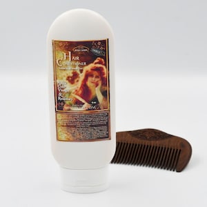 May include: White bottle of hair conditioner with a vintage label featuring a woman with red hair. The label reads "Hair Conditioner Leave-in Treatment" and "Apple Cider Vinegar & Rosemary". The bottle is next to a wooden comb.