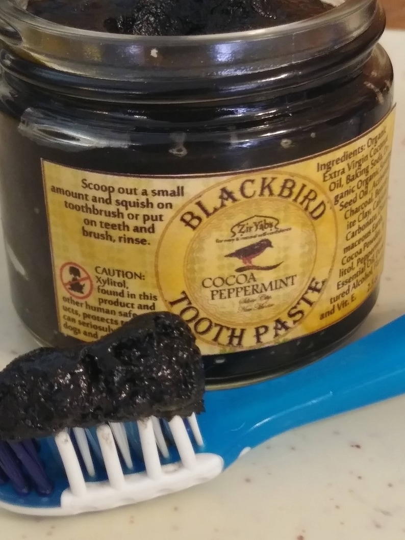 Peut inclure: Un pot en verre de dentifrice &agrave; la menthe poivr&eacute;e et au cacao Blackbird Zir Yabs. Le pot est jaune et noir avec un logo d'oiseau noir. Le dentifrice est de couleur charbon fonc&eacute;. Une brosse &agrave; dents bleue avec une t&ecirc;te de poils blancs a une noisette de dentifrice dessus.