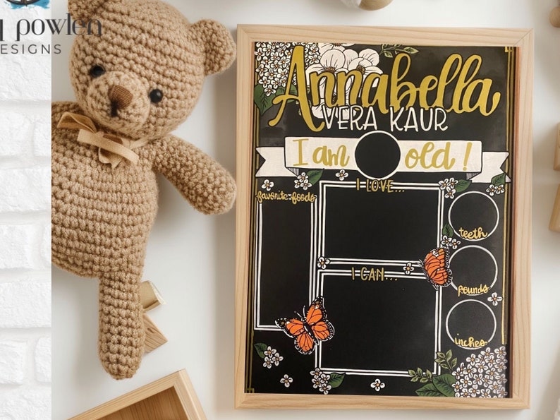 May include: A black chalkboard with a floral design and gold accents. The text "Annabella Vera Kaur I am old!" is written on the board. There are sections for favourite foods, things I love, things I can do, teeth, pounds, and inches.