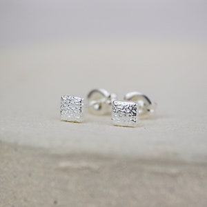 May include: A pair of silver square stud earrings with a textured surface.
