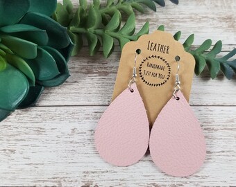 May include: A pair of pink leather teardrop earrings with silver hooks. The earrings are on a brown card with the text "Leather Handmade Just For You".