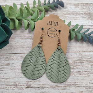 以下が含まれることがあります： 編み込み模様の入った緑色の革の雫型のイヤリングのペア。イヤリングは手作りで、銅製のフックが付いています。