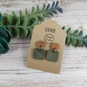 May include: A pair of green suede leather earrings with wooden and gold accents. The earrings are displayed on a card that reads "Leather Handmade Just For You".