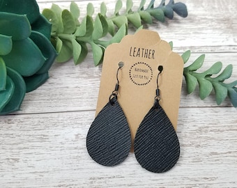 May include: A pair of black leather teardrop earrings with silver hooks. The earrings are on a brown card with the text "Leather Handmade Just For You".