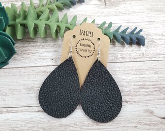May include: Black leather teardrop earrings with silver hooks. The earrings are handmade and have a textured surface. The tag says "Leather Handmade Just For You".