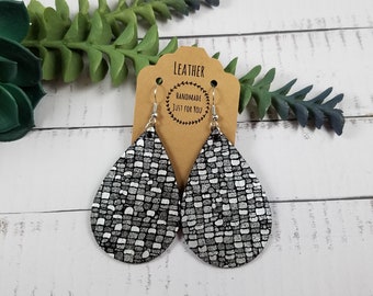 May include: A pair of teardrop-shaped leather earrings with a black and silver snakeskin pattern. The earrings are handmade and have silver hooks.