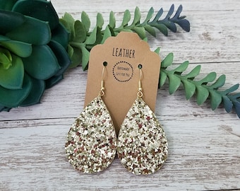May include: Gold glitter teardrop earrings with gold hooks. The earrings are handmade and have a tag that says "Leather Handmade Just for You".