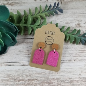 May include: A pair of pink suede earrings with wooden tops. The earrings are displayed on a card that says "Leather Handmade Just for You".