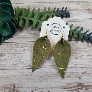 May include: A pair of green cork earrings with gold flecks. The earrings are shaped like teardrops and have a hook closure. The earrings are handmade and are labeled "Handmade Just For You".