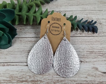 May include: Silver teardrop shaped leather earrings with silver hooks. The earrings are handmade and come with a tag that says "Leather Handmade Just For You".