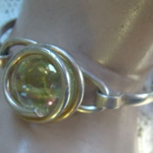 May include: A silver bangle bracelet with a large, round, iridescent green gemstone set in a silver bezel.