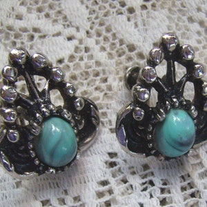 May include: A pair of silver tone earrings with a turquoise stone set in a decorative design.