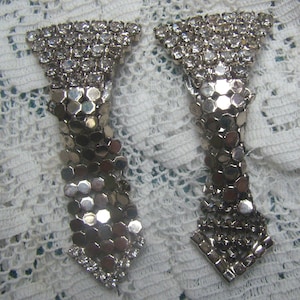 May include: A pair of silver tone rhinestone and chain belt buckles. Each buckle features a triangular top with rhinestones and a chain link design.